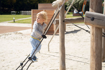 Little caucasian blond boy playing on kids playground in a sunny autumn day