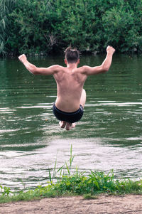 Rear view of shirtless man jumping in lake