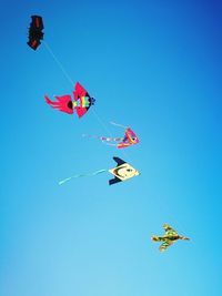 Low angle view of kites flying against clear blue sky