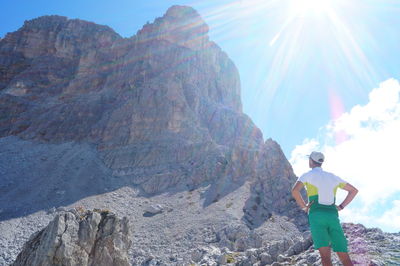 Rear view of man with hands on hip standing against rocky mountains