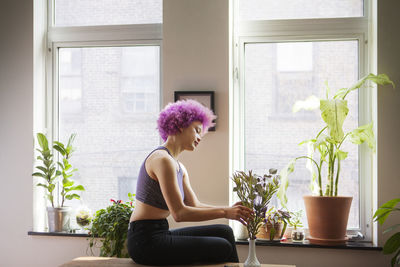 Side view of woman keeping plant in vase at home