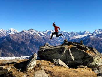 Man jumping on snowcapped mountain against sky