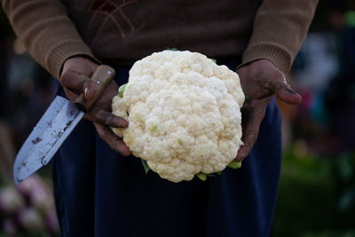 A man in vegetable market showing cauliflower to customers.