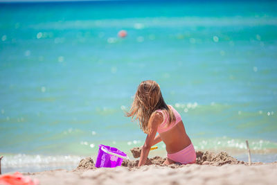 Rear view of young woman sitting at beach against sky