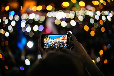Cropped hands of man photographing illuminated protest at night