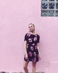 Young woman in floral pattern dress standing by pink wall