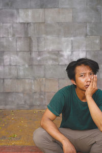 Young man sitting against wall