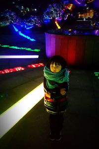 Portrait of smiling girl standing at illuminated shop