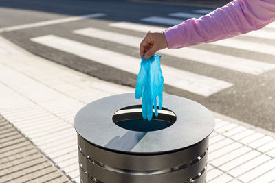 Female hand throwing out a protective glove into the trash can of the street. coronavirus or covid-19 waste concept
