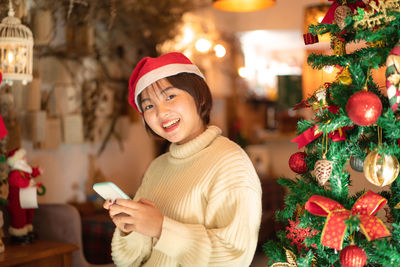 Portrait of smiling woman using mobile phone against christmas tree