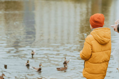 A boy in a yellow jacket feeds ducks on the lake, copy space. feeding the ducks with bread. 