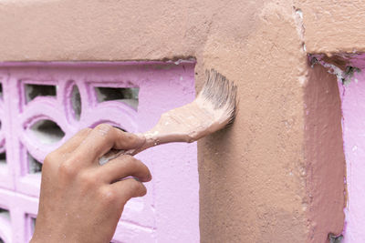 Cropped hand of male painter painting brown paint on wall
