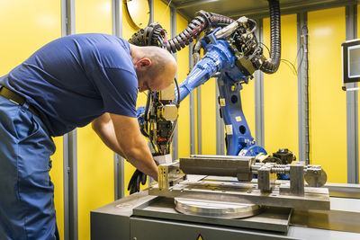 Maintenance engineer working with blue robotic arm in modern factory