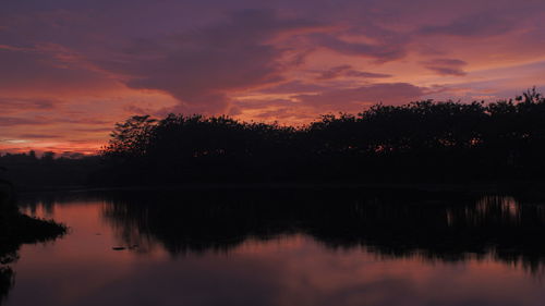 Silhouette trees by lake against sky during sunset