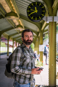 Portrait of mid adult man using phone at railroad station platform