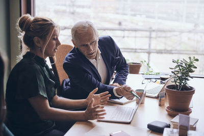 Confident mature businessman discussing over laptop with businesswoman during meeting at creative office