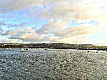 Boats sailing in sea against cloudy sky