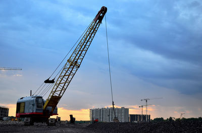 Cranes at construction site against sky during sunset