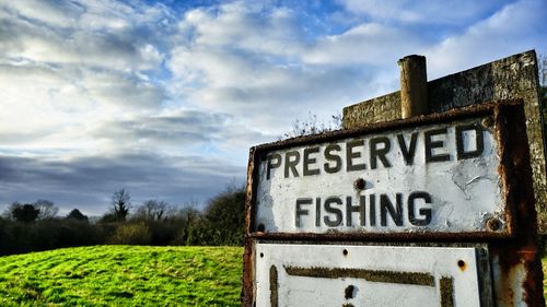 Close-up of rusty sign on field against sky
