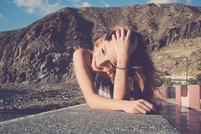 Woman with hand in hair lying on retaining wall