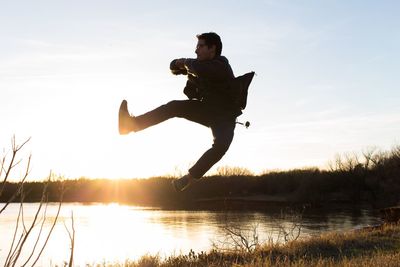 Man jumping in lake against sky during sunset