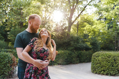 Happy friends standing by plants against trees