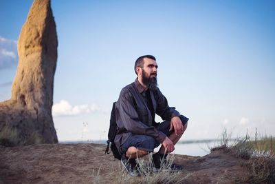 Young man sitting on land against sky