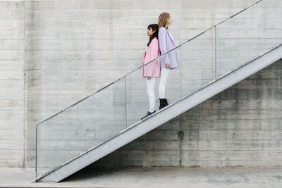 Young siblings back to back standing on steps by wall