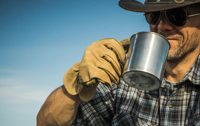 Low angle view of man holding coffee cup against blue sky