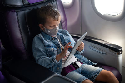 A boy in a medical mask sits in an airplane seat.  traveling safely during the coronavirus pandemic