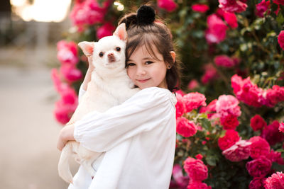 Pretty little child girl 4-5 year old hold chihuhua pet dog posing over flower background close up