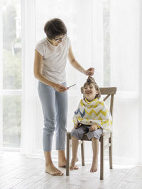 Mother cuts her son's hair by herself. little boy sits, covered with cloth, holds pair of scissors. 