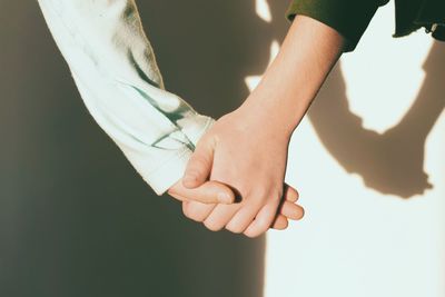 Cropped image of couple holding hands against wall