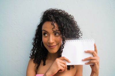 Portrait of beautiful woman holding camera against wall