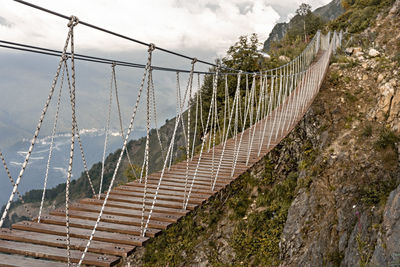 Suspended wooden bridge hanging over an abyss in mountain canyon and clouds, extreme hike 