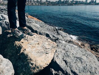 Low section of person standing on rock by sea