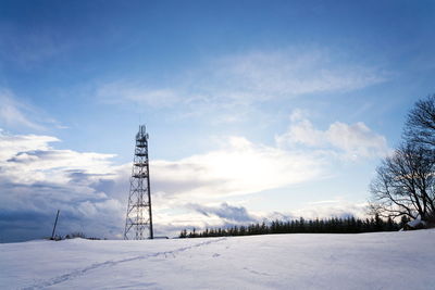 Electricity pylon on snow covered field against sky