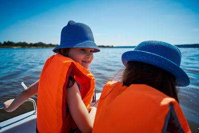 Girls wearing life jackets sitting in boat against clear blue sky