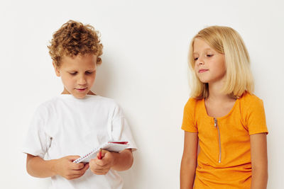 Boy with notebook standing by girl against white background