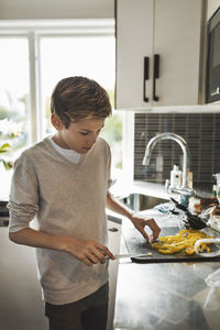 Boy cutting yellow bell pepper at kitchen counter