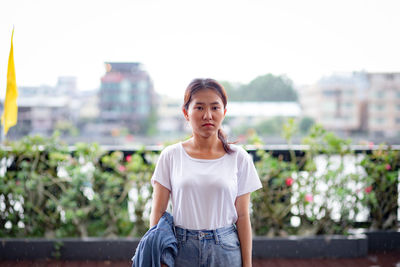 Portrait of young woman standing against city in background