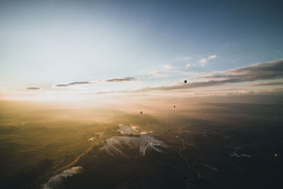 Hot air balloons flying over foggy landscape against sky during sunrise