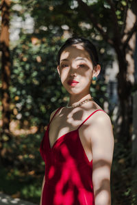 Portrait of a young woman standing outdoors in shadows of trees