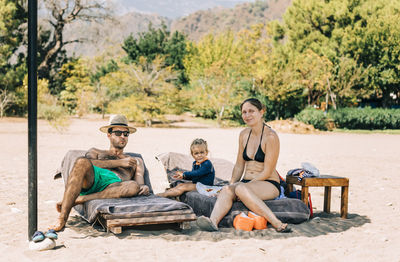 Family relaxing at beach against trees