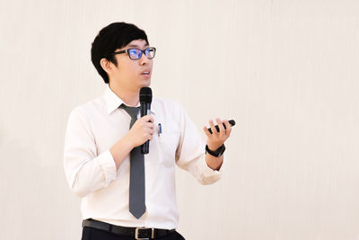 Young man holding camera while standing against white background