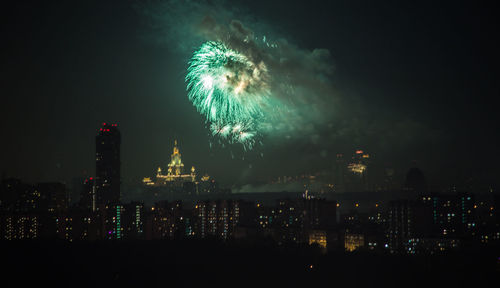 Firework display in city against sky at night