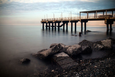 Pier over river against sky during sunset