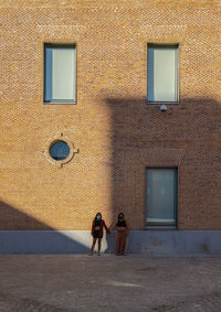 Two young girls with mask standing against brick wall