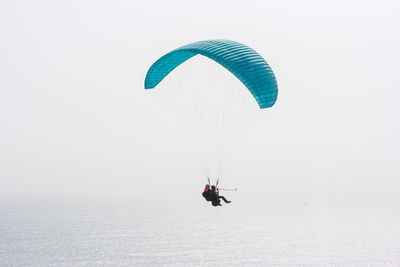 High angle view of people paragliding over ocean against clear sky