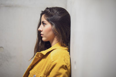 Side view of young woman standing against wall